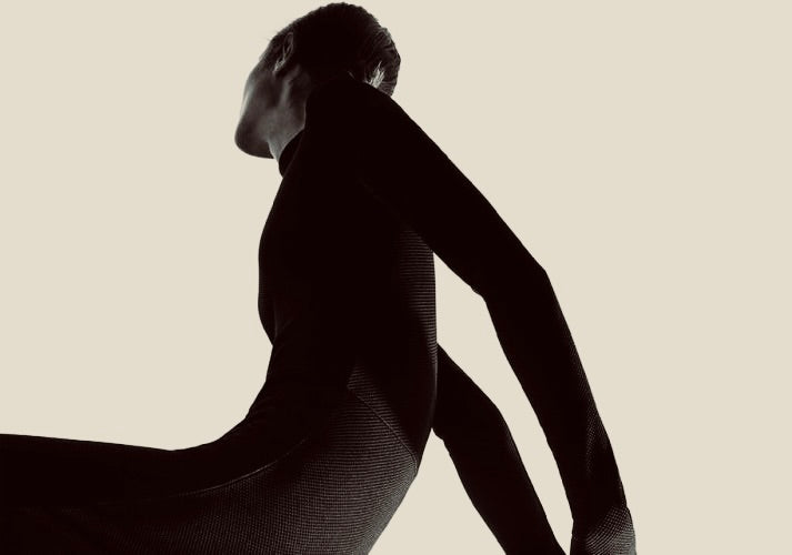 Person in a black bodysuit performing a split against a beige background